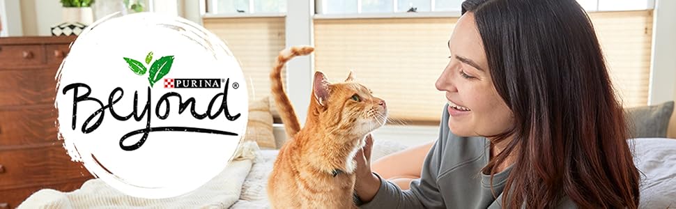 A woman and her cat lay on a bed. The woman smiles as she pets the cat.